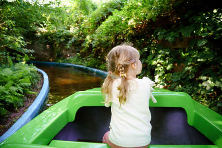 Adorable little toddler girl riding on boat carousel in amusement park. Happy healthy baby child having fun outdoors on sunny day. Family weekend or vacationsの写真素材