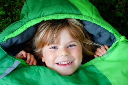 Preschool little girl in sleeping bag camping. Outdoors activity with children in summer. Fun and...
