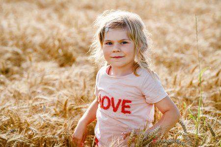 Portrait of happy smiling preschool girl in wheat grain field outdoors. Little child with blond...