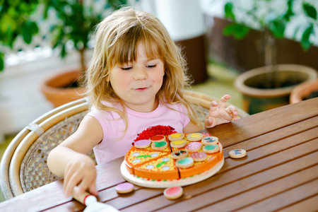 Little cute girl playing with wooden toy pizza. Preschool child having fun with children activity like, play with food, indoors.の写真素材