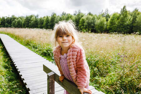 Little girl walking on wooden path on black moor nature landscape. Active preschool child exploring National Park with trees, plants, boggy landscape.の写真素材
