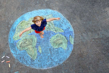 Little preschool girl with earth globe painting with colorful chalks on ground. Positive toddler child. Happy earth day concept. Creation of children for saving world, environment and ecology.の写真素材