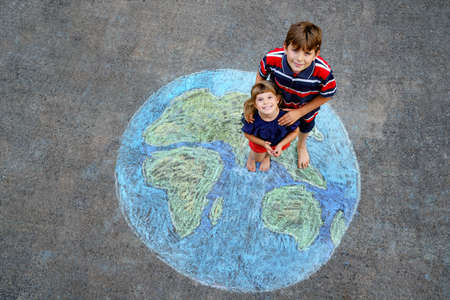 Little preschool girl and school kid boy with earth globe painting with colorful chalks on ground. Happy earth day concept. Creation of children for saving world, environment and ecology.の写真素材