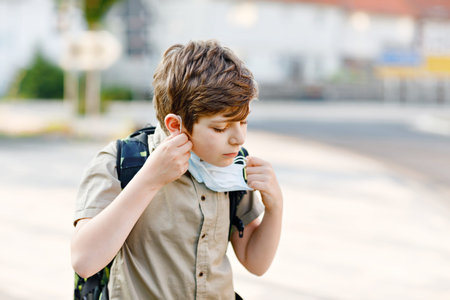 Happy kid boy with glasses and medical mask due to virus pandemic. Schoolkid with satchel waiting...