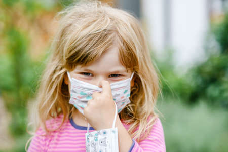 Little toddler girl on her first day on way to playschool with medical mask against  virus. Sad and upset preschool child walking to nursery preschool and kindergarten.の写真素材