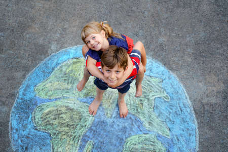 Little preschool girl and school kid boy with earth globe painting with colorful chalks on ground. Happy earth day concept. Creation of children for saving world, environment and ecology.の写真素材