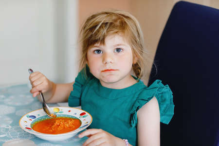 Little preschool girl eating healthy vegetable tomato soup for lunch. Cute happy child taking food at home or nursery daycare or kindergarten. Healthy meal for children with fresh vegetables.の写真素材