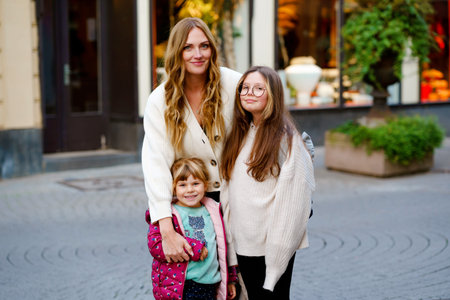 Young mother, school preteen girl and preschool child making walk in the city. Happy family, woman...