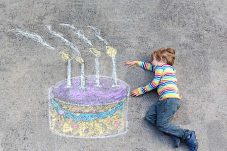 Happy little kid boy having fun with big birthday cake picture drawing with colorful chalks. Creative leisure activity for children outdoors in summer. Child celebrating birthday and drawing on groundの写真素材