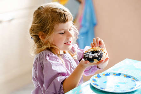 Happy little preschool girl eating sweet donut indoor. Blond child in the city. Cute kid and unhealthy sugared food doughnut.の写真素材