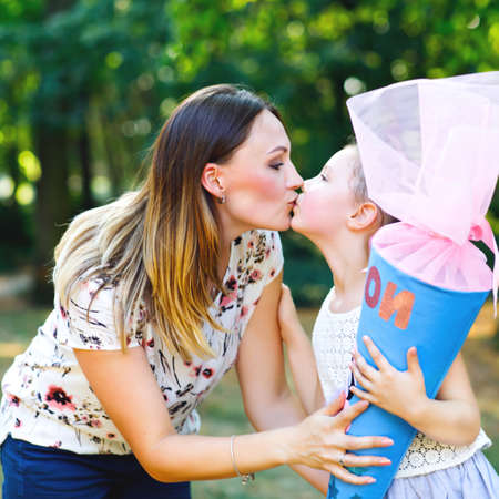 Happy little kid girl and mother with big traditional school gift cone in Germany. schoolkid on first day of elementary class. Back to school concept. Healthy child and woman kissing and hugging,の写真素材