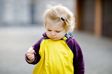 Cute adorable toddler girl playing outdoors on spring day. Baby child wearing yellow mud rain puddle pants trousers. Portrait of happy girl.の写真素材