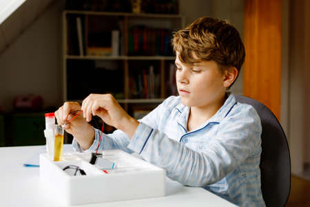 Preteen kid boy doing electric physical experiment as homework at home. Child study electricity. Education. Kids learning physics.の写真素材