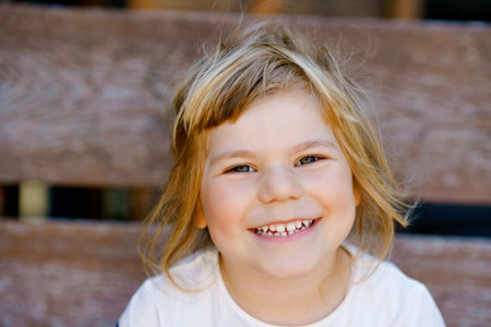 Portrait of happy smiling toddler girl outdoors. Little child with blond hairs looking and smiling...