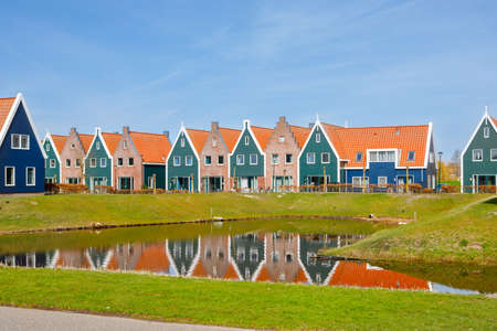 Panorama with modern brick houses along water in a family friendly suburban neighborhood in Volendam in the Netherlands. Typical Dutch houses and windmill on background.の写真素材