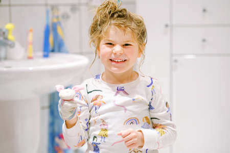 Cute preschool girl in pajamas after taking bath. Happy smiling child with wet long hair playing with toy socks, having fun. Healthy hygiene routine for children.の写真素材