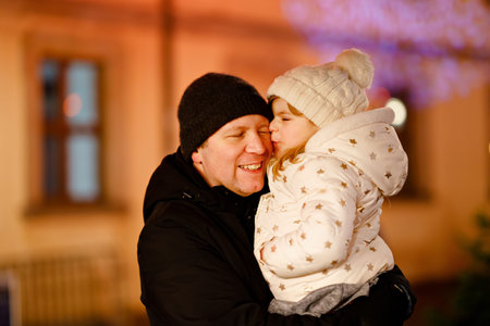 Little preschool girl sitting on shoulder of father on Christmas market in Germany. Happy toddler...