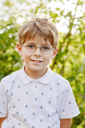 Outdoor portrait of little cute school kid boy with glasses and colorful school uniform fashion...