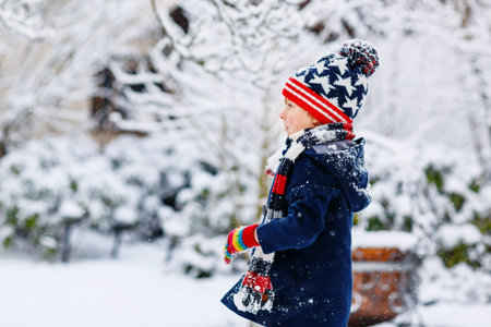 Funny little kid boy in colorful clothes playing outdoors during strong snowfall
