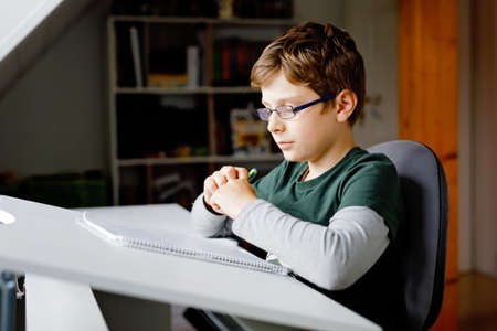 Kid boy with glasses learns at home for school. Preteen child making homework. Home schooling and distance learning concept.の写真素材