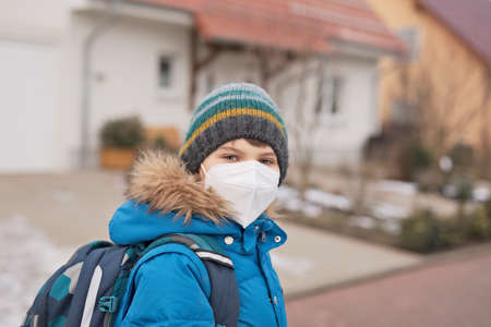 Kid boy wearing ffp medical mask on the way to school. Child backpack satchel. Schoolkid on cold autumn or winter day with warm clothes. Lockdown and quarantine time during corona pandemic diseaseの写真素材