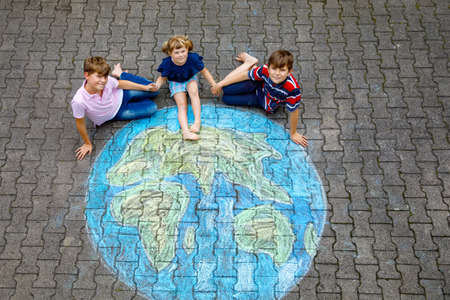 Little preschool girl and two school kids boys with earth globe painting with colorful chalks on ground. Happy earth day concept. Creation of children for saving world, environment and ecology.の写真素材