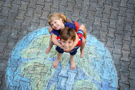 Little preschool girl and school kid boy with earth globe painting with colorful chalks on ground. Happy earth day concept. Creation of children for saving world, environment and ecology.の写真素材