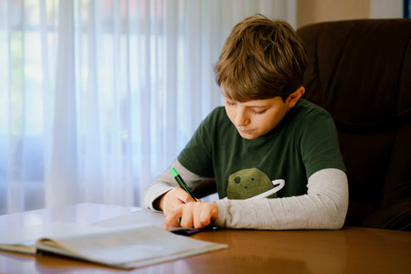 Hard-working happy school kid boy making homework during quarantine time from corona pandemic...