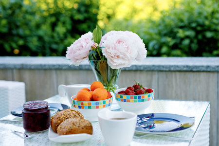 Breakfast table with bread, fresh fruits and strawberries and coffee served on balkony terrace or...
