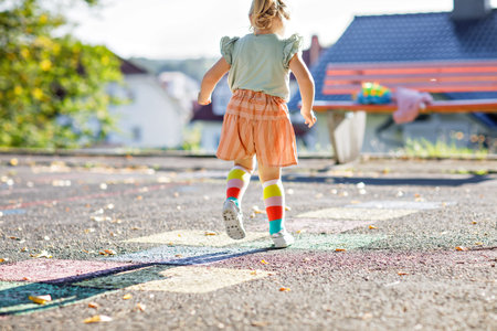 Closeup of leggs of little toddler girl playing hopscotch game drawn with colorful chalks on...