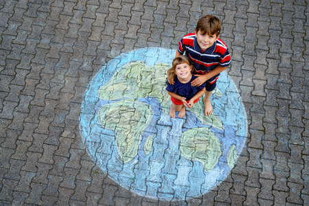 Little preschool girl and school kid boy with earth globe painting with colorful chalks on ground. Happy earth day concept. Creation of children for saving world, environment and ecology.の写真素材