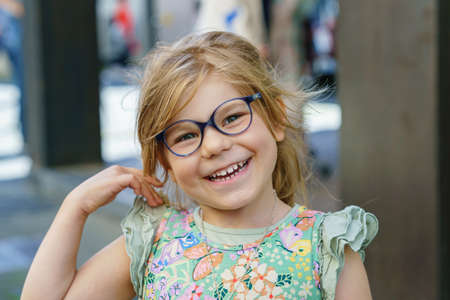 Portrait of a cute preschool girl with eye glasses outdoors. Happy funny child wearing new blue glasses.の写真素材