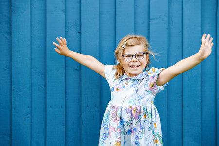 Portrait of happy smiling toddler girl in blue clothes outdoors. Little child with blond hairs...