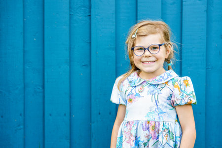 Portrait of happy smiling toddler girl in blue clothes outdoors. Little child with blond hairs looking and smiling at the camera. Happy healthy child enjoy outdoor activity and playing.の写真素材
