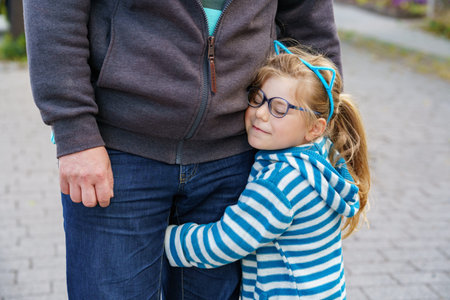 Happy child preschool girl smiles and holds fathers hand on the way to school on the first sunny day of class. Dad and daughter on the way to kindergarten, fun together. Child with glasses.の写真素材