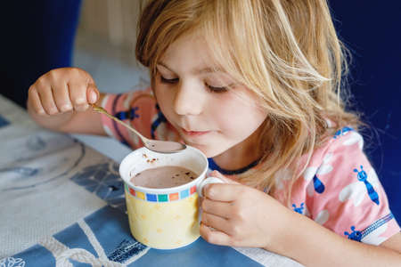 Adorable girl drinking hot chocolate in domestic kitchen. Happy preschool child.の写真素材