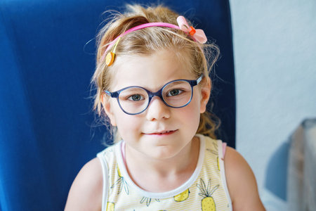 Portrait of a cute preschool girl with eye glasses indoors. Happy funny child wearing new blue glasses.の写真素材