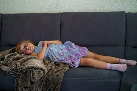 Little girl watching TV lying on couch. Preschool child with glasses enjoying cartoons or film.の写真素材