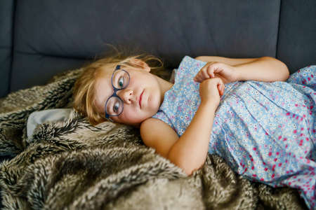 Little girl watching TV lying on couch. Preschool child with glasses enjoying cartoons or film.の写真素材