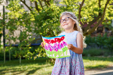 Little preschool girl holding picture painted with colorful water colors. Happy child with glasses,...