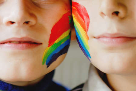 Two kid boys with painted rainbow with colorful colors on face during pandemic coronavirus quarantine. Children make and paint rainbows around the world. Siblings, best friendsの写真素材