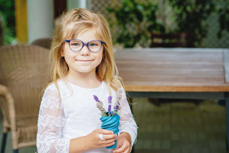 Little preschool girl with flower lavender bouquet at home. Happy child holding a small vaseの写真素材
