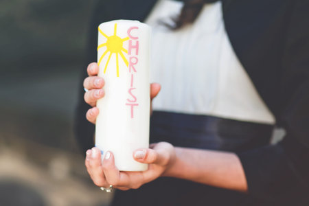Hands of girl holding candle with crucifix for holy confirmation or communion.