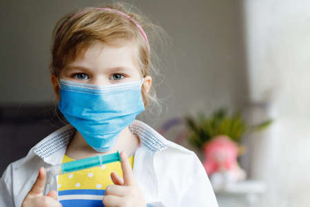 Little girl makes injection. Cute child with medical mask playing doctor, holding syringe with vaccine.の写真素材