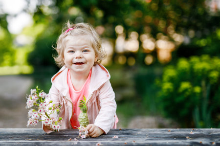 Cute adorable toddler girl playing with blooming chestnut flowers. Little baby child going for a...