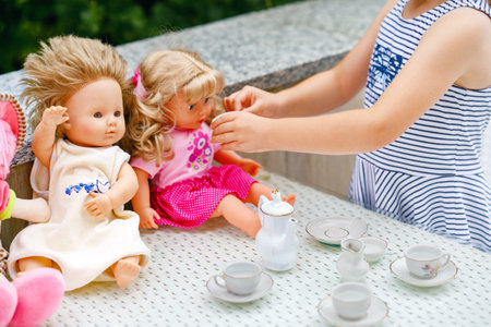 Little preschool girl playing with dolls. Happy excited child play tea party with toys. Role games for children, activity for one person. Role game for small children.の写真素材