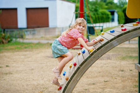 Little girl climbing on playground on summer day. Happy brave preschool child enjoying sports and children activity.の写真素材