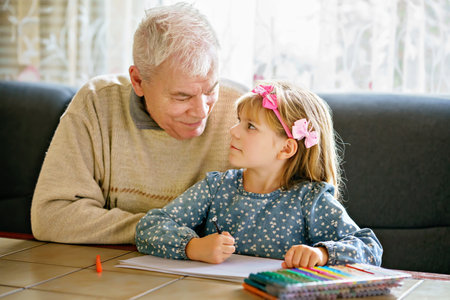 Cute little preschool girl and handsome senior grandfather painting with colorful pencils at home. Grandchild and man having fun togetherの写真素材