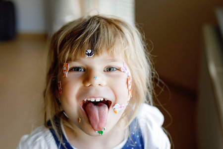 Little toddler girl playing with different colorful animal stickers. Concept of activity of children during pandemic corona virus quarantine. Happy funny child having fun with stick stickers on face.の写真素材