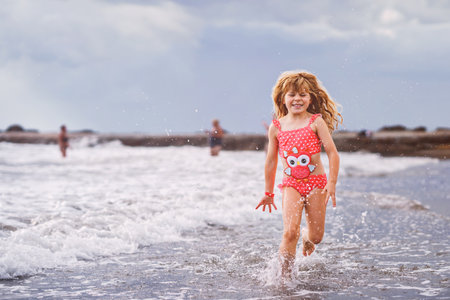 Happy child, little preschool girl running and jumping in the waves during summer vacation on exotic tropical beach. Family journey on ocean coastの写真素材